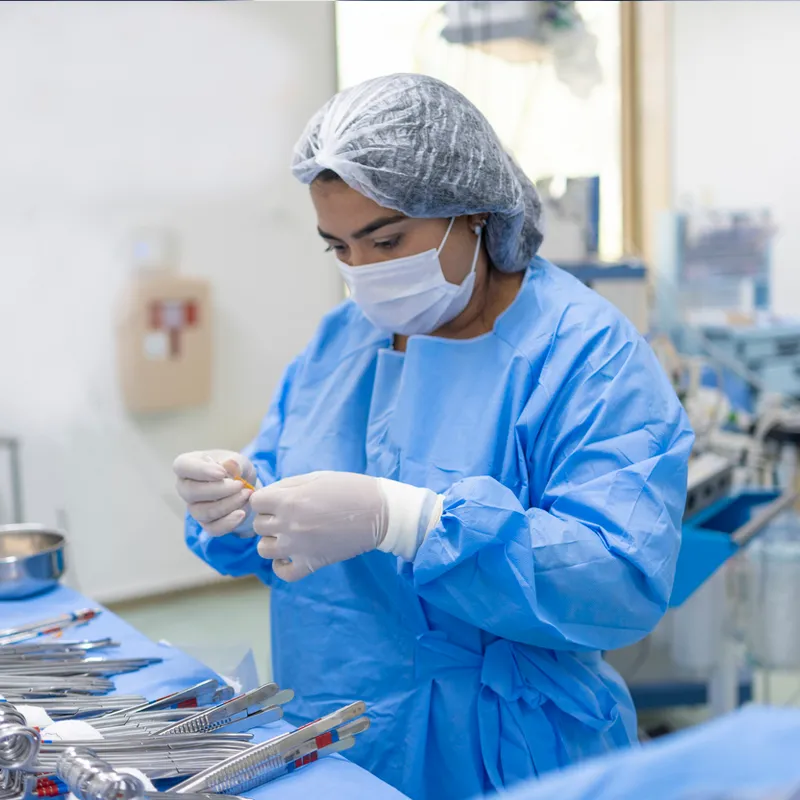 Person in blue surgical gown, hair cover, and gloves sorting medical instruments on a sterile table.