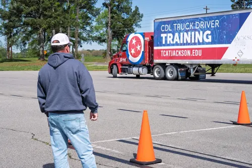 Two people stand beside a semi‑truck with the hood open, looking at engine components during hands‑on instruction.